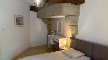 A bedroom with a bed, a desk, and a chair, a mirror, and a hanging light fixture.