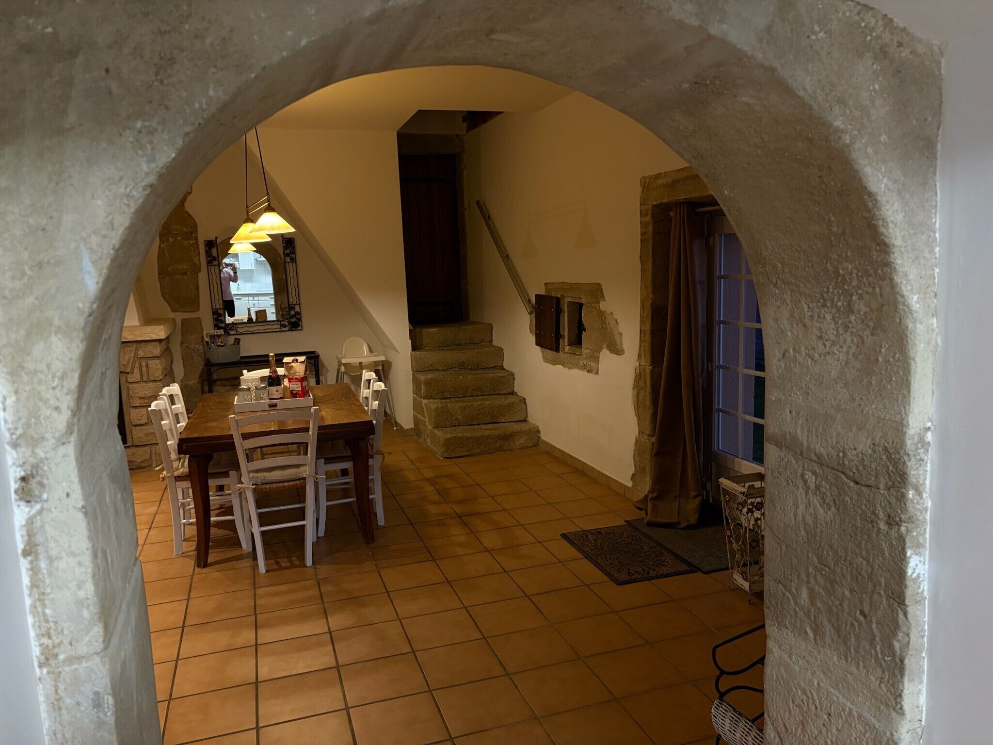 Un comedor con mesa y sillas, una escalera y un arco de piedra.