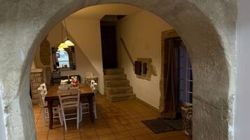 Un comedor con mesa y sillas, una escalera y un arco de piedra.