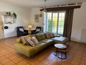 Una sala de estar con un sofá verde, dos sillones, una mesita redonda y una lámpara colgante.