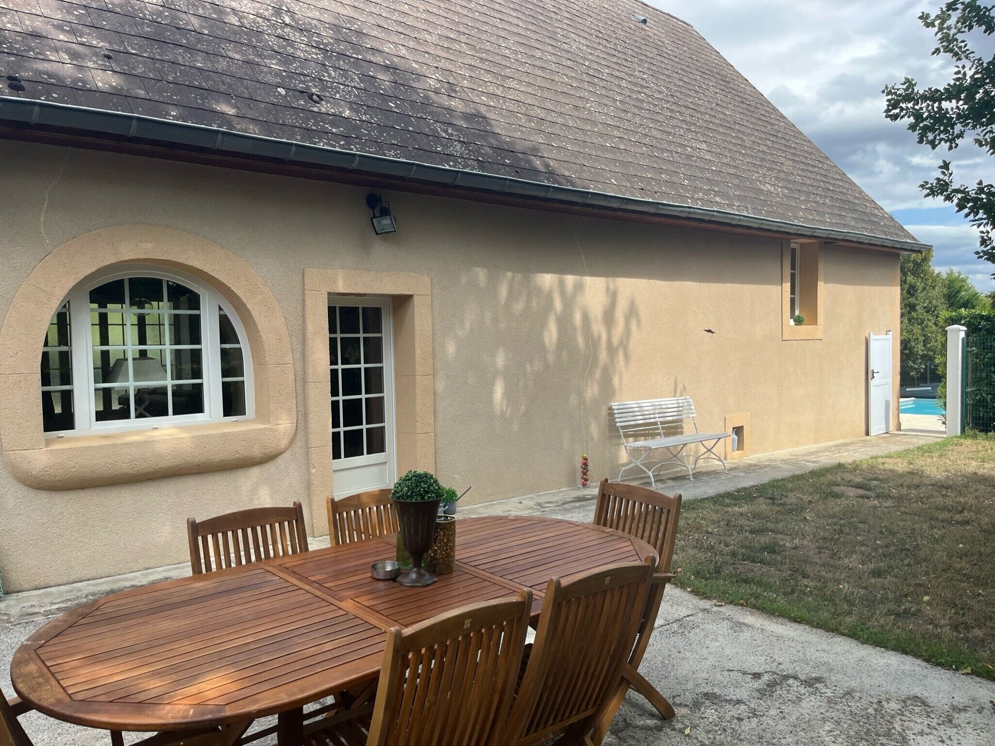 Une maison dotée d’un patio couvert, d’une table à manger avec des chaises et d’un petit jardin.