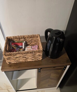 A woven basket containing tea bags and a black coffee maker on a wooden surface. - Tropical Oasis: Cozy 1- bedroom with AC near JFK Airport, LIRR Train (Queens)