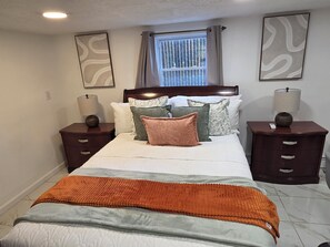 Quarto com cama, duas mesas de cabeceira, janela com cortinas e decoração nas paredes.