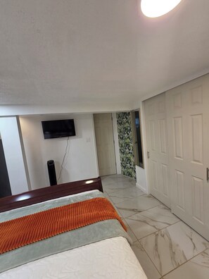 A bedroom with a bed, a television mounted on the wall, a door, and a patterned wallpaper section. - Tropical Oasis: Cozy 1- bedroom with AC near JFK Airport, LIRR Train (Queens)