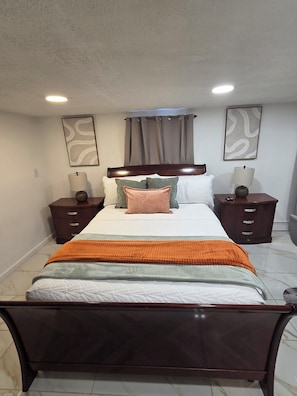 A bedroom with a bed, two nightstands, a headboard, a window with curtains, and two wall-mounted lamps. - Tropical Oasis: Cozy 1- bedroom with AC near JFK Airport, LIRR Train (Queens)