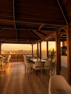 A covered outdoor dining area with a city view, featuring wooden flooring and a mix of table and chair styles. - Casablanca Pyramids View Hotel (Giza)