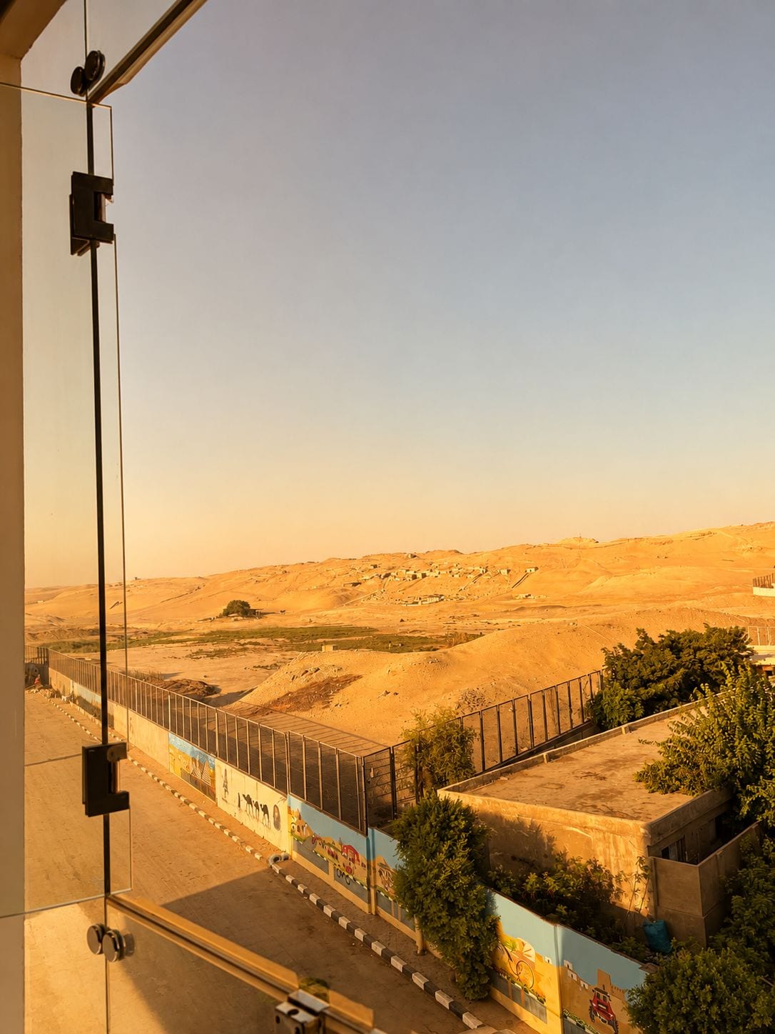 Paisatge desert amb una zona tancada per una tanca i un edifici amb un mural.