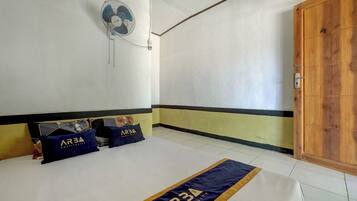 Een hotelkamer met een bed, een wandventilator en een houten deur.