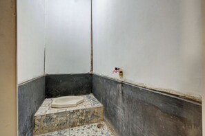 A small, enclosed bathroom with a tiled floor, a bathtub, and a wall-mounted faucet.