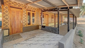 Un espacio al aire libre cubierto con suelo de baldosas, puertas de madera con diseños decorativos y una estructura de techo metálico.