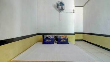 A hotel room with a bed, pillows, a wall-mounted fan, and a bedside table.