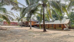 Zona arenosa con palmeras y edificios de madera, posiblemente un resort o propiedad vacacional.