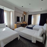 Habitación de hotel con dos camas individuales, un escritorio y un televisor de pantalla plana, y un ventanal con cortinas.