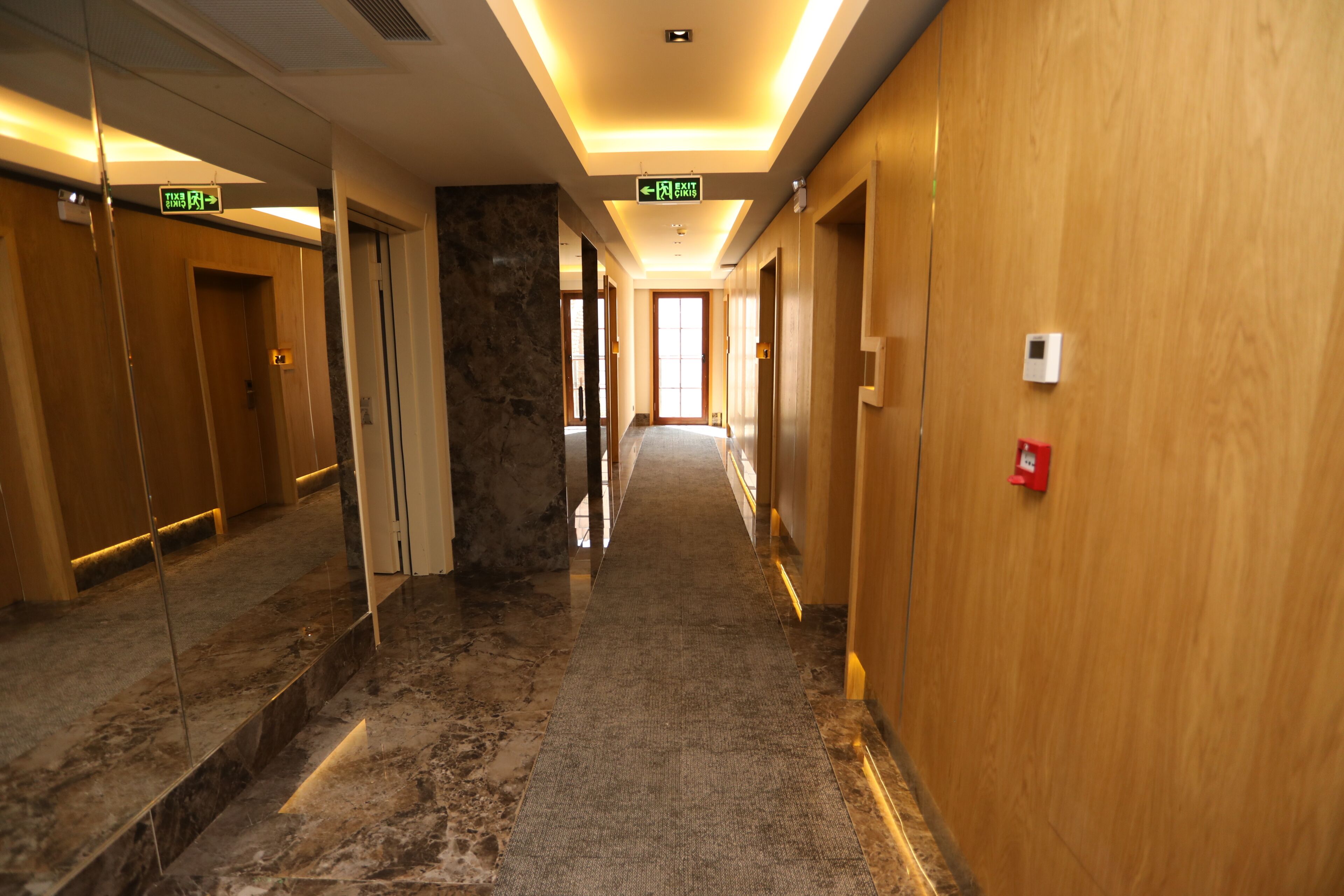 A hotel corridor with marble flooring, wooden walls, and exit signs.