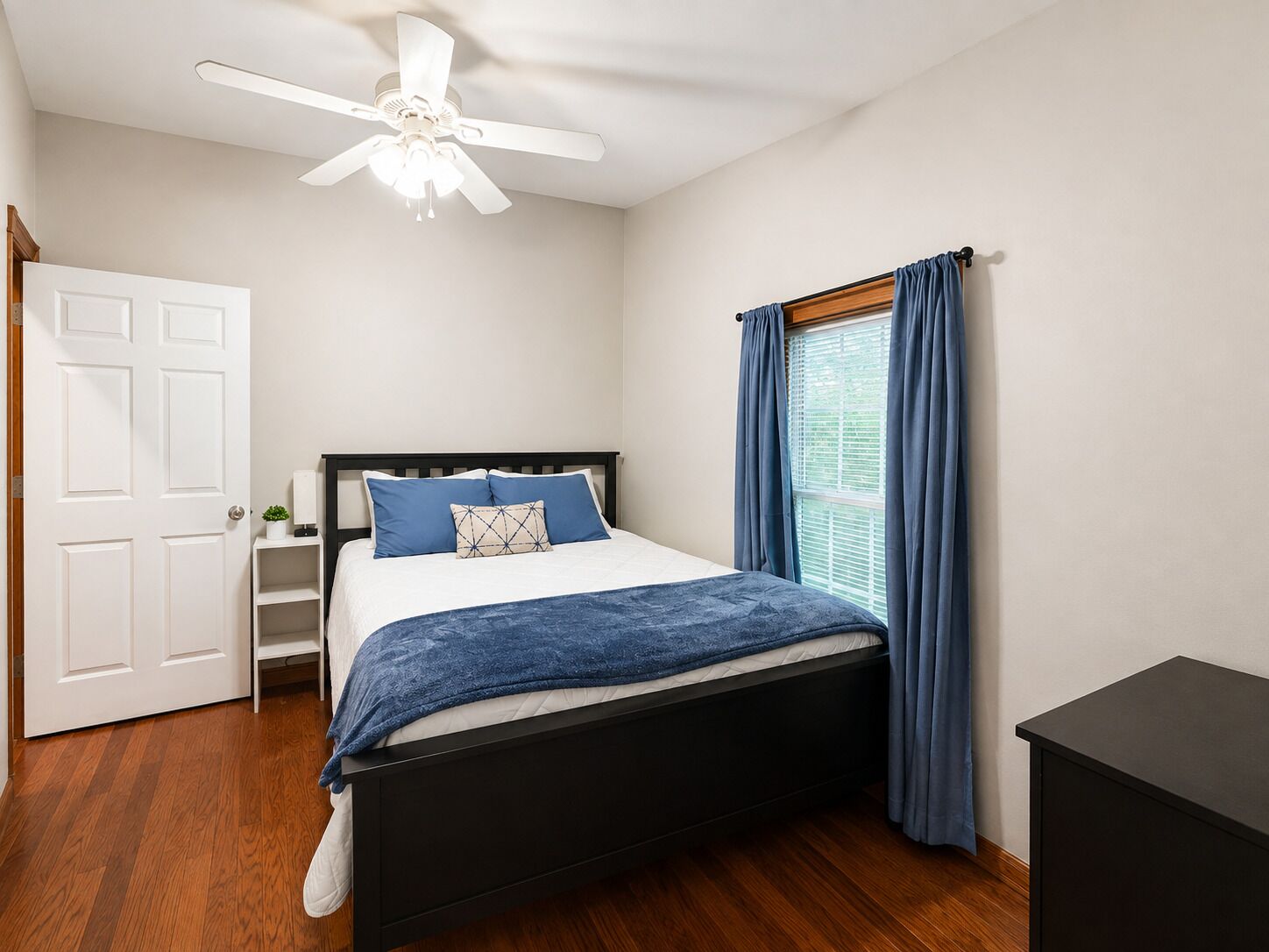 Une chambre à coucher avec un lit, un ventilateur de plafond, une fenêtre avec des rideaux et une porte.