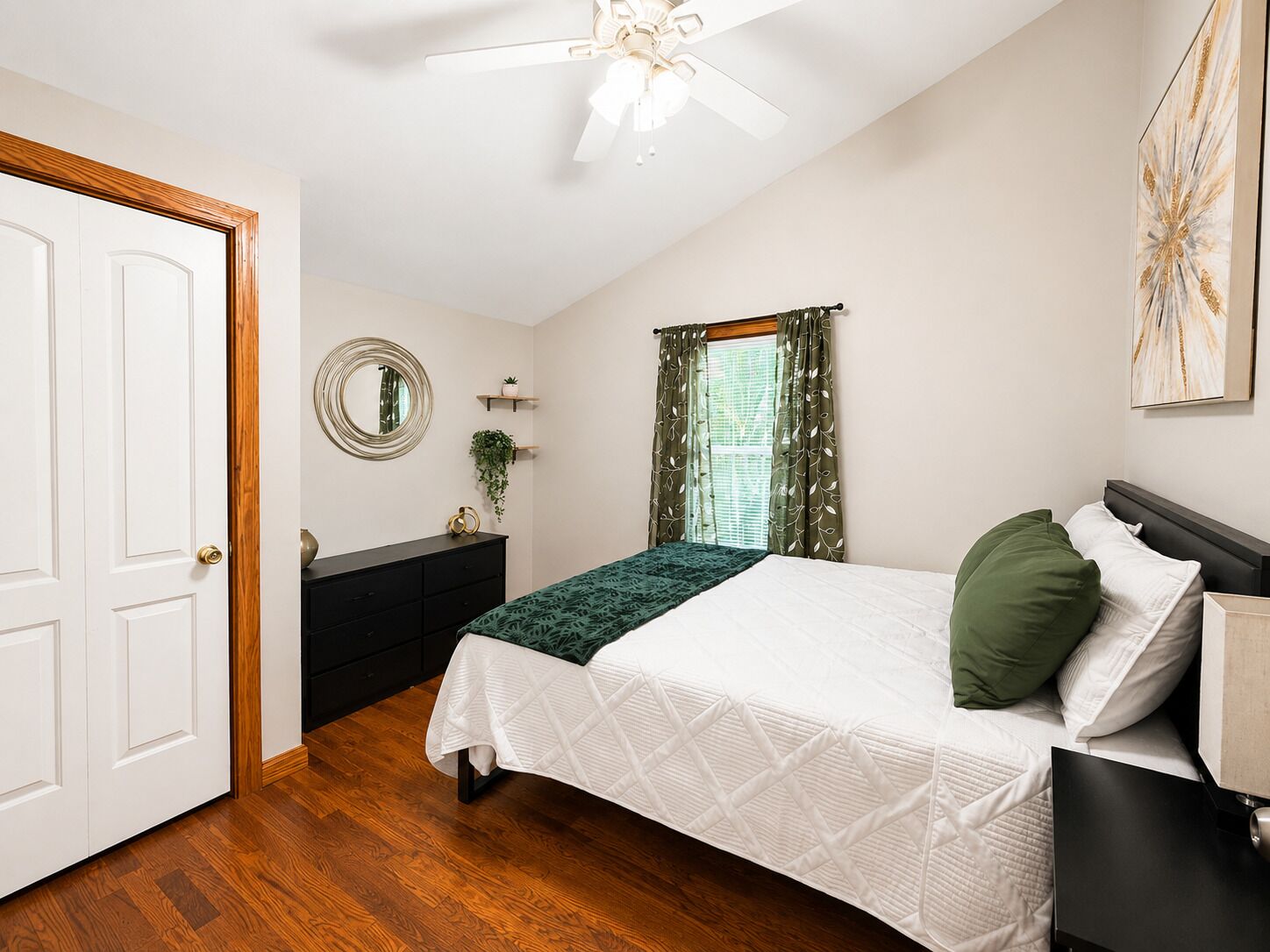 A bedroom with a bed, a dresser, a mirror, a window with curtains, and a ceiling fan.
