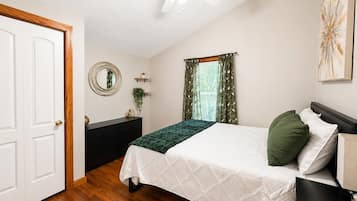 A bedroom with a bed, a dresser, a mirror, a window with curtains, and a ceiling fan.