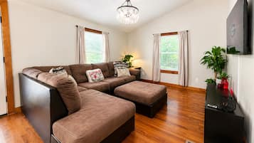 A modern living room with a sectional sofa, a small table, a chandelier, and a flat-screen TV.