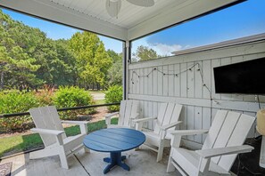 Ein überdachter Sitzbereich mit Tisch und Stühlen, mit Blick auf einen Garten mit Bäumen und Sträuchern.