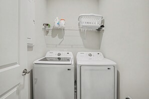A laundry room with two white washing machines and a shelf above holding a basket and a bottle. - New on Program! The Townes at Barefoot #5202! Your Favorite Place to Golf! (North Myrtle Beach)