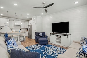 A modern living room with a sofa, armchair, and a flat-screen TV mounted on a wall. - New on Program! The Townes at Barefoot #5202! Your Favorite Place to Golf! (North Myrtle Beach)