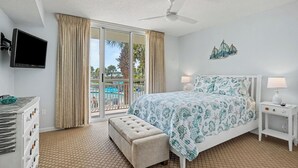 Una habitación de hotel con cama, televisión, balcón y vista a la piscina, además de ventilador de techo.