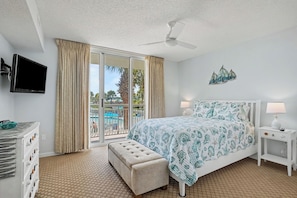 Ein Hotelzimmer mit Bett, Fernseher, einem Balkon mit Blick auf den Pool und einem Deckenventilator.