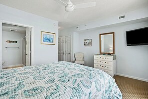 Ein Schlafzimmer mit einem Bett, einem Schminktisch, einem Sessel, einem Fernseher und einer Tür zu einem weiteren Raum.