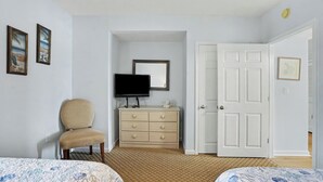 Una habitación con cama, una silla, cómoda, televisor y puerta.