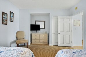 Ein Zimmer mit Bett, Stuhl, Kommode, Fernseher und einer Tür.