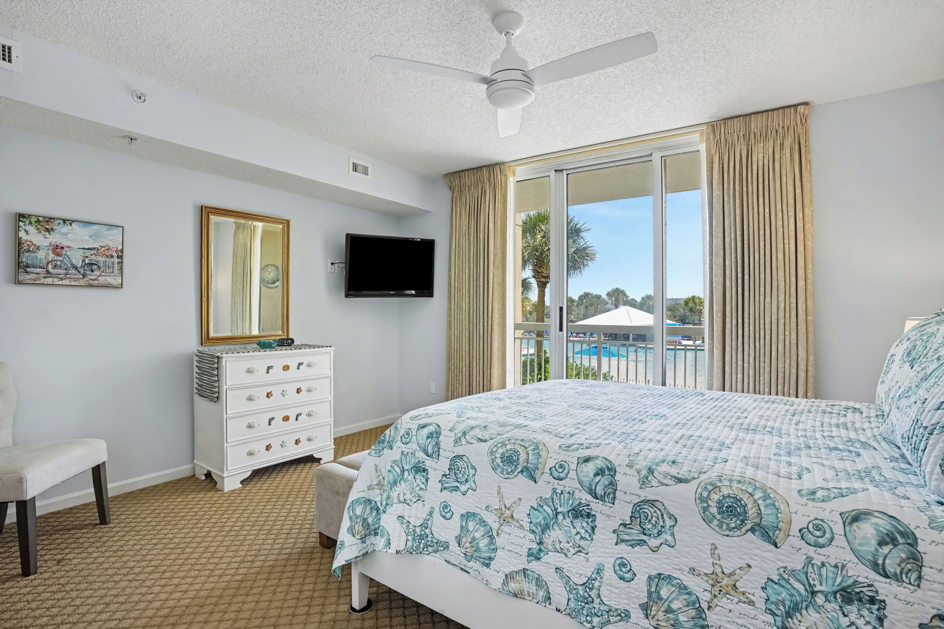 A hotel room with a bed, a dresser, a television, a ceiling fan, and a window with curtains.