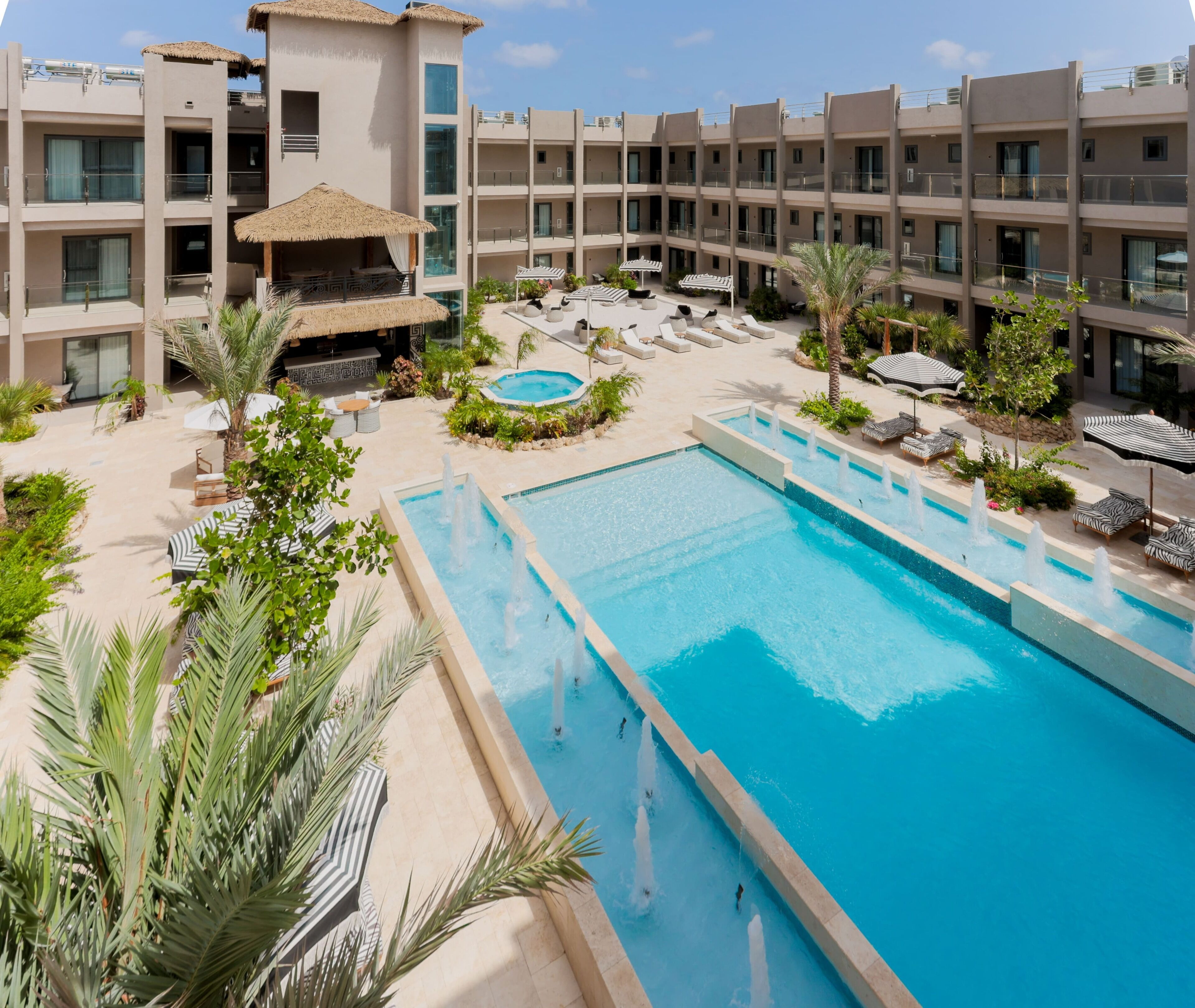 A hotel with a large pool, lounge chairs, and a small waterfall feature.