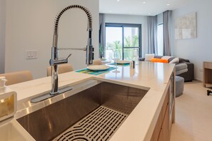 A modern kitchen with a stainless steel sink, a built-in oven, and a dining area with a table set for two. - Modern Condo Near Eagle Beach-Balcony, Pool & Gym, Brand new Walishali Condo (Oranjestad)
