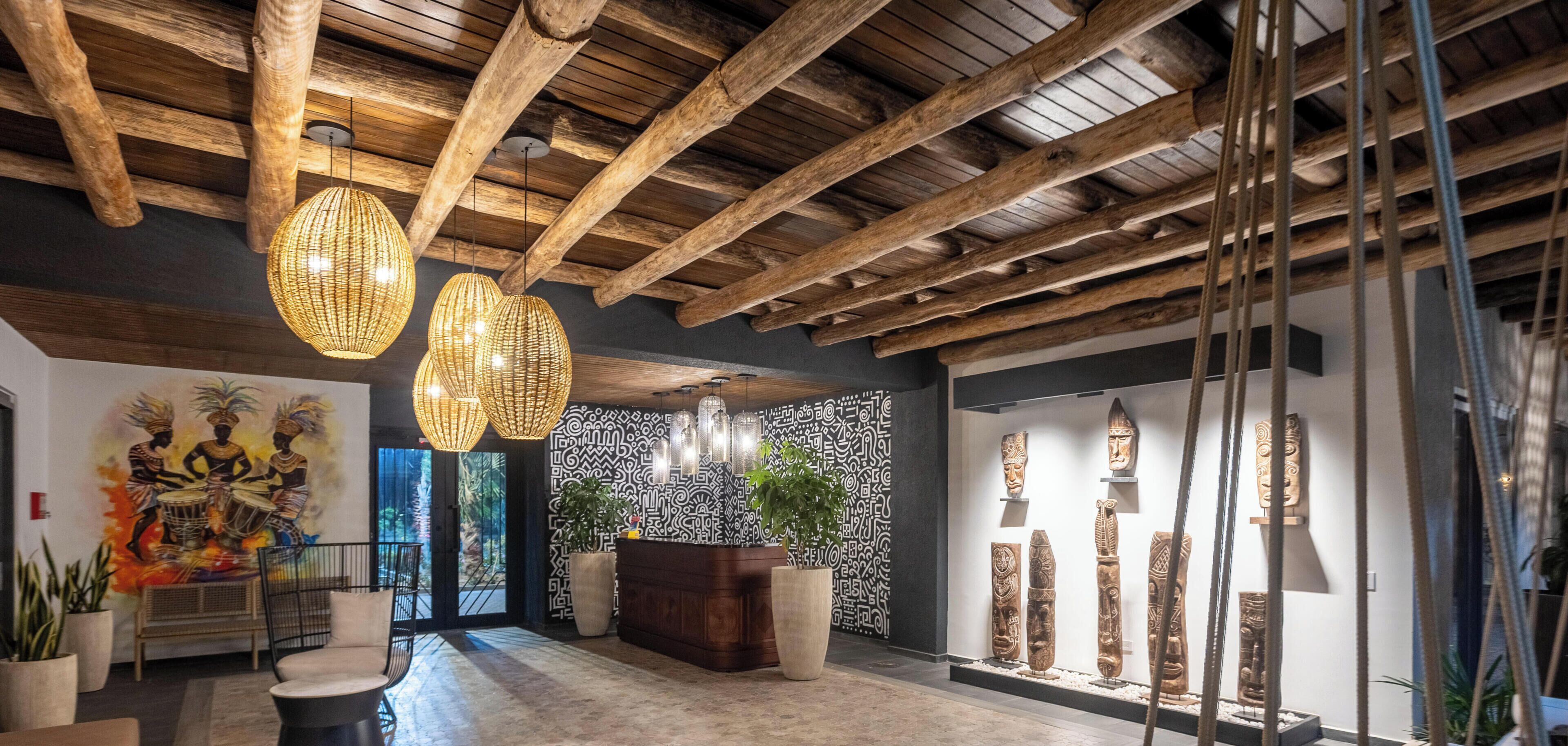 A lobby with wooden beams, woven light fixtures, a reception desk, and a wall with carved sculptures.