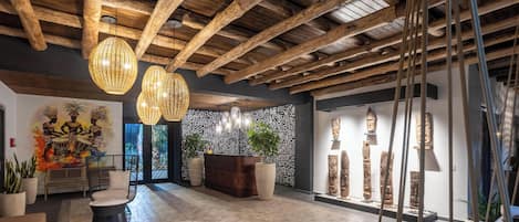 Un vestíbulo con vigas de madera, lámparas de fibra, una recepción y una pared con esculturas talladas.
