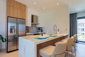 A modern kitchen with a central island, stainless steel appliances, and a view of the outdoors. - Modern Condo Near Eagle Beach-Balcony, Pool & Gym, Brand new Walishali Condo (Oranjestad)