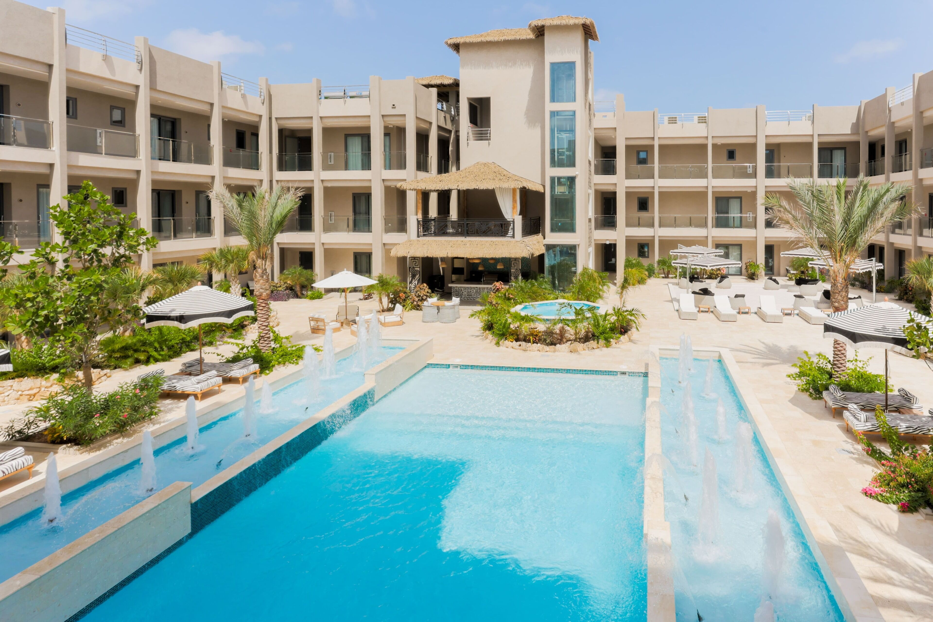 A hotel with a central swimming pool, multiple balconies, and outdoor seating areas.