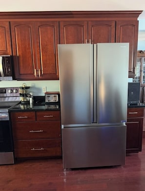 A stainless steel refrigerator in a kitchen with wooden cabinets and a microwave.