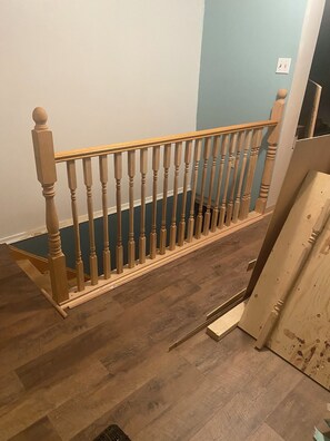 Eine Holztreppe mit Geländer, Holzbalken und einem dunklen Boden.