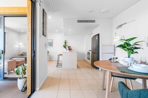 Eine moderne Küche mit einer zentralen Kochinsel, einem Essbereich mit Holztisch und einem Wohnbereich mit Sofa und Pflanze.