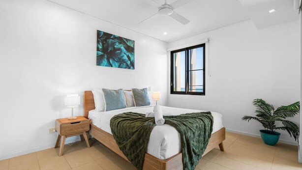A bedroom with a bed, nightstand, lamp, window, and a ceiling fan. - Zen Botanica Waterfront Sea View Pool Quiet (Darwin)