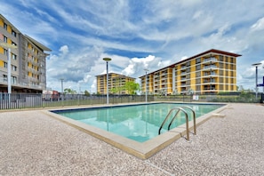 Ein Pool mit Metallleiter, umgeben von Kiesflächen, mit mehrstöckigen Gebäuden im Hintergrund.