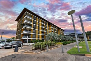 A multi-story building with balconies, a parking area, and a landscaped garden.