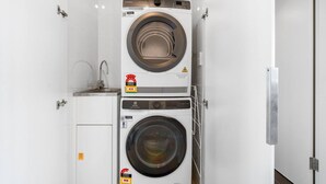 A compact laundry area with two stacked washing machines, a small sink, and a detergent bottle. - Zen Botanica Waterfront Sea View Pool Quiet (Darwin)