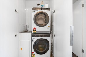 A compact laundry area with two stacked washing machines, a small sink, and a detergent bottle.