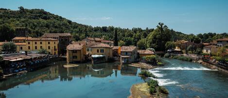 A riverside town with buildings along the water, a bridge, and a hill in the background.