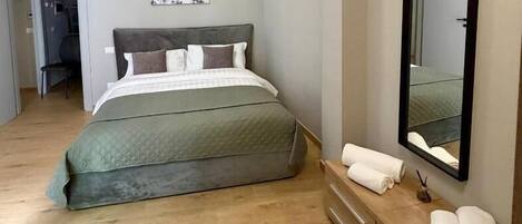 Un dormitorio con cama, cómoda, espejo y puerta que da a otra habitación.