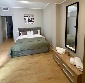 A bedroom with a bed, a dresser, a mirror, and a door leading to another room.