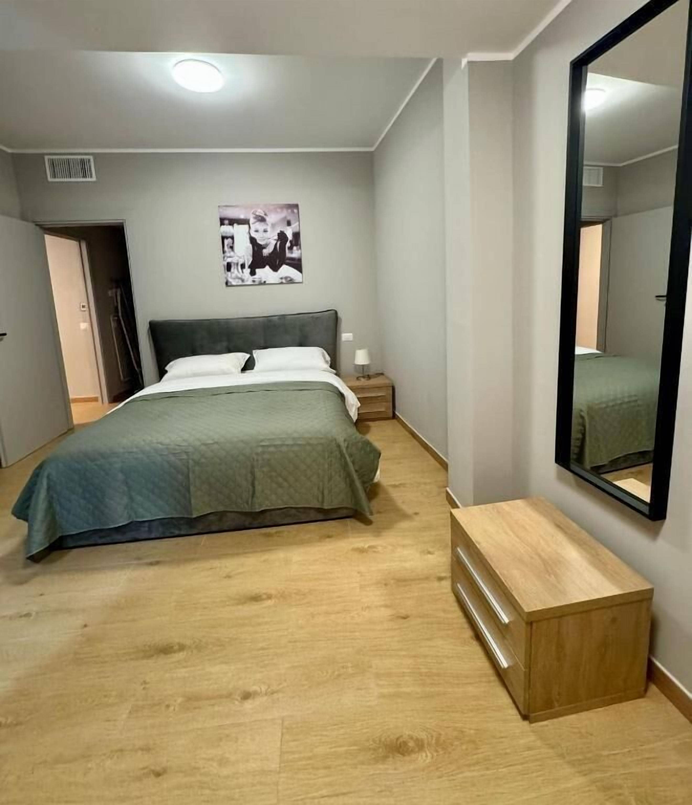 A bedroom with a bed, bedside table, mirror, and a wall-mounted picture.