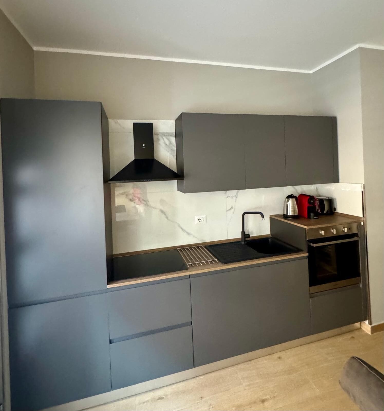 Una cocina moderna con encimera negra, pileta de acero inoxidable y horno empotrado.